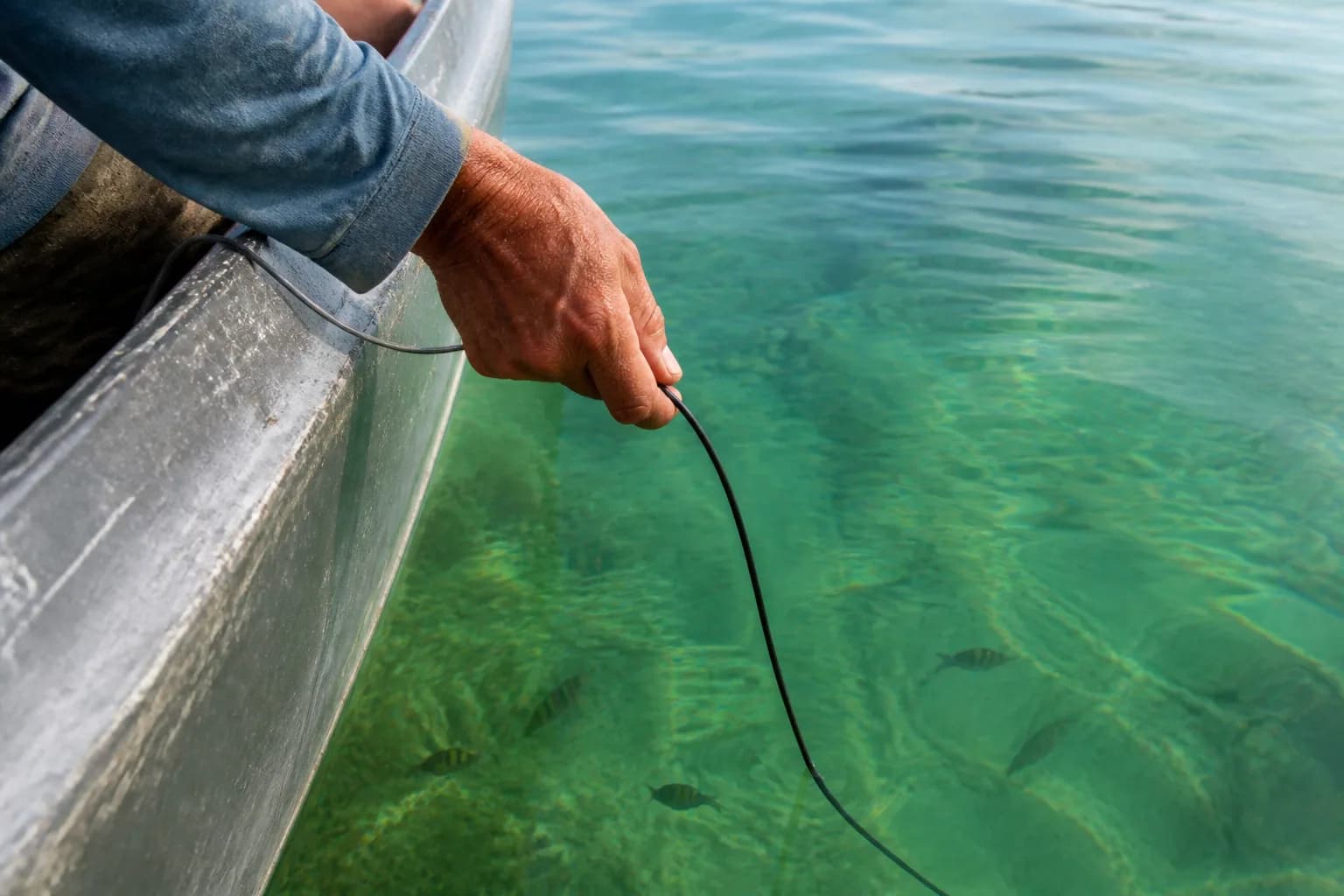 Close view of an angler guiding an underwater camera cable into emerald Florida water